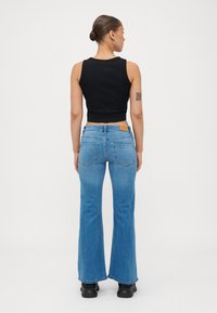 Svart avkortet tanktopp parret med blå flagrende jeans. Funksjoner inkluderer en beige etikett på baklivet og teksturert denim.