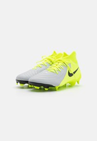 Nike futbola apavi pelēkā krāsā ar spilgti dzelteniem akcentiem. Iezīmējas ar strukturētu augšdaļu, saistēšanas dizainu un melnu zoli ar dzelteniem dūrieniem.