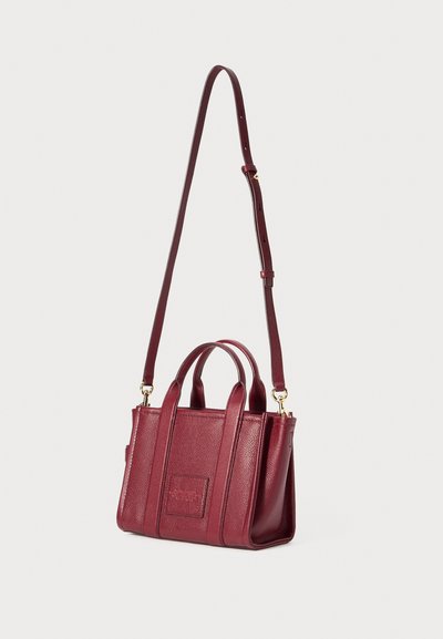 Burgundy leather handbag with textured surface, dual top handles, detachable shoulder strap, and gold hardware accents.