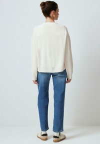 Crème-kleurige gebreide trui met een cropped ontwerp, geribbelde zoom, losse mouwen, gecombineerd met lichtblauwe rechte jeans en beige sneakers.
