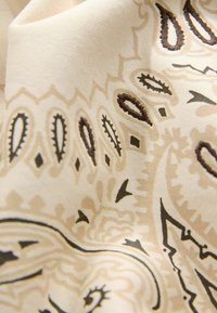 Cream fabric with intricate brown paisley and geometric patterns; smooth texture, lightweight, draping softly with subtle sheen.