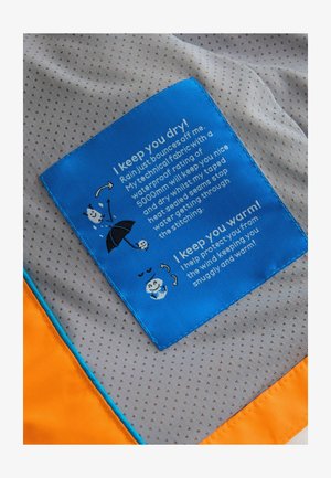 Etichetă din material textil albastru cu instrucțiuni de îngrijire; conține text și ilustrații pe un fundal gri deschis, punctat, cu accente portocalii pe margine.