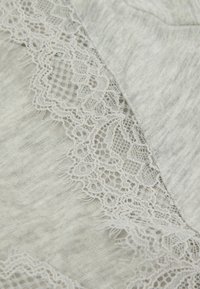 Světle šedá tkanina s jemným bílým krajkovým lemem na jedné straně. Textura je měkká s jemným melírovaným vzorem. Krajka má složité detaily.