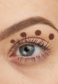 Close-up van een mensenoog met een blauwe iris en opvallende wimpers, met drie bruine stippen op het wenkbrauwbot boven het ooglid.