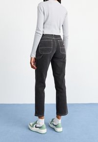 Vaqueros de mezclilla negra con un ajuste entallado, que cuentan con dos bolsillos traseros y costuras en contraste. Combinados con zapatillas blancas y verdes.