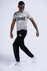 Gray T-shirt with black "Lonsdale" graphic and black sweatpants. White athletic shoes. Casual, comfortable fit, designed for movement.