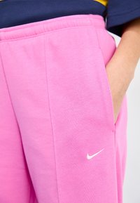Roze joggingsbroek met een zachte textuur, voorzien van een wit Nike-logo aan de linkerkant en een zijzak voor gemak.