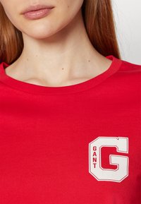 Rode katoenen t-shirt met een ronde halslijn, voorzien van een wit "GANT" logo en de letter 'G' in een contrasterend grafisch ontwerp op de borst.