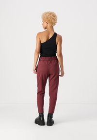 Top nero a spalla unica abbinato a pantaloni bordeaux a sigaretta con elastico in vita e tasche posteriori, indossato con stivali neri con tacco alto.