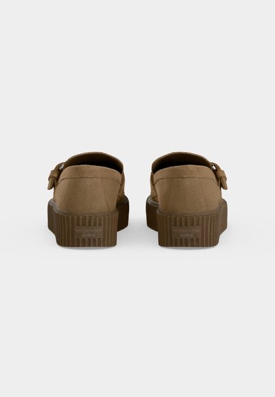 Paire de mocassins en daim marron avec des semelles épaisses en caoutchouc, vus de dos sur un fond clair uni.