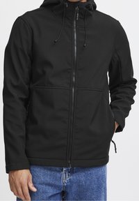 Veste softshell noire à fermeture éclair devant, capuche ajustable et deux poches latérales. Présente une texture lisse et des poignets élastiques.