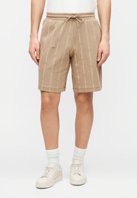 Smėlio spalvos šortai su elastinga juosmens juosta ir raišteliais, su pasikartojančiu baltos spalvos logotipo raštu, pagaminti iš minkštos, tekstūruotos medžiagos.