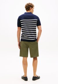Marineblå polo med hvide striber, korte ærmer; kombineret med khaki shorts og mørke sko, set bagfra.