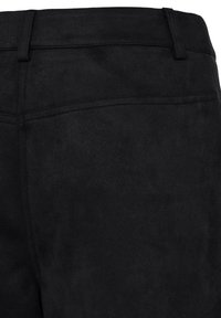 Gros plan d’un pantalon en daim noir montrant la ceinture, les passants de ceinture et les détails des coutures de la poche arrière.