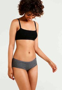 Bralette preta e elástica com alças finas, combinada com calções estilo boxer cinzentos. Os tecidos são suaves, com textura lisa e design minimalista.