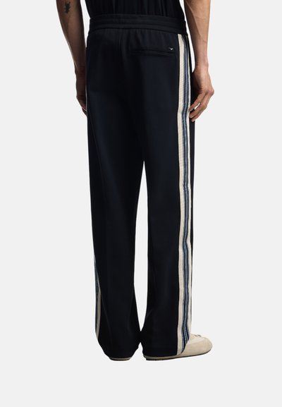 Svarta träningsbyxor med en avslappnad passform, med grädde- och blå sidostråkar samt en bakfickdetailj. Mjuk tyg med en slät textur.