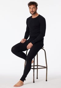 Top nero a maniche lunghe e leggings attillati realizzati in un tessuto morbido e elastico. Il top presenta un collo rotondo, mentre i leggings hanno polsini aderenti.