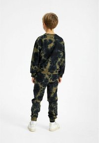 Set di felpa e pantaloni jogger tie-dye verde e nero, con polsini e vita a costine, abbinato a sneakers bianche.