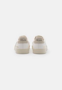 Hvite sneakers med beige mocka hæl-akkenter. Har merkevarenavnet "VEJA" på hælen. Glatt lær overdel, gummisåle.