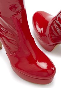 Red patent leather ankle boots with a smooth, shiny finish, a chunky heel, and a rounded toe. Features a side cutout for design accents.
