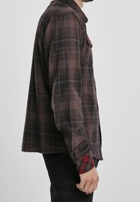 Chemise en flanelle à carreaux bordeaux foncé et noir, présentant une coupe décontractée, une fermeture à boutons et des accents de poignets à carreaux rouges.