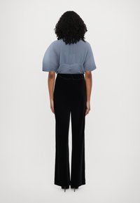 Top plissé bleu clair à manches courtes, associé à un pantalon large en velours noir, vu de derrière. Textures lisses, design minimaliste.