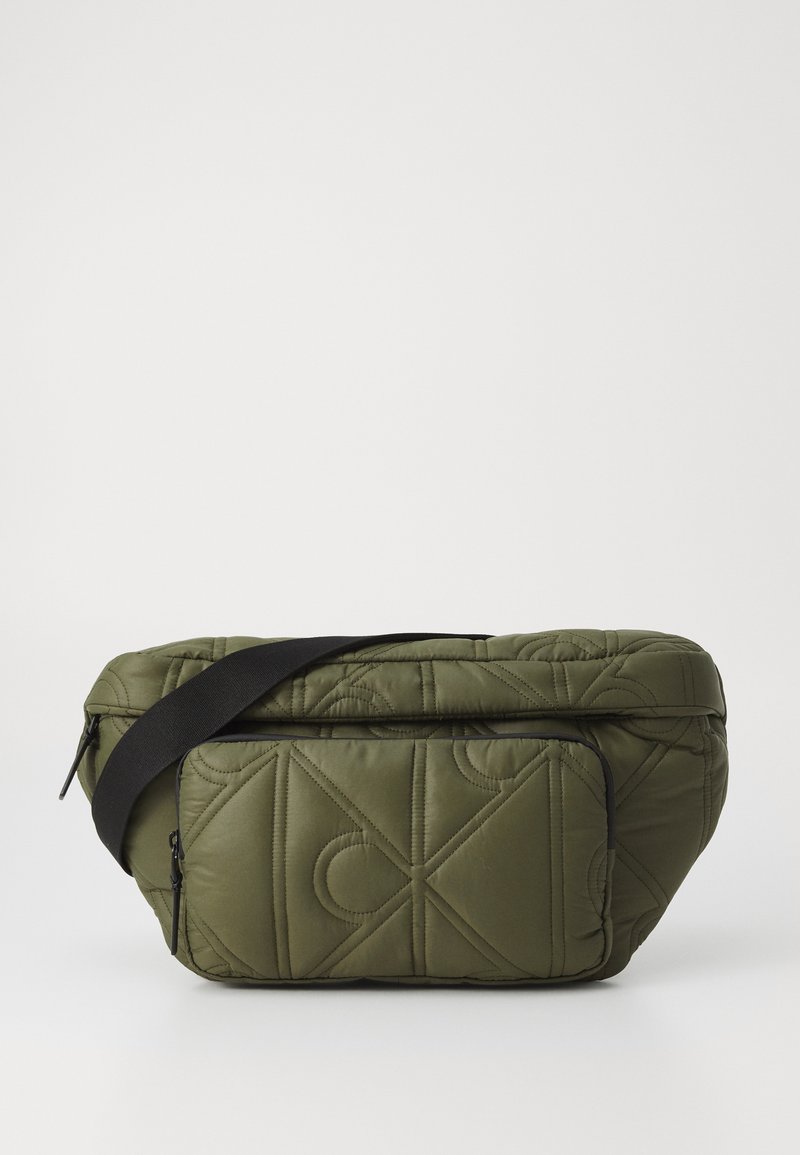 Bolso de hombro acolchado en color verde oliva con una correa negra. Presenta un bolsillo con cremallera en la parte frontal y una textura suave y acolchada.