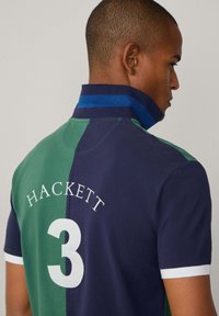 Polo tričko v zelené a námořnické barvě, s vysokým límcem modrými pruhy, bílými akcenty, logem "HACKETT" a velkým "3" na zadní straně.
