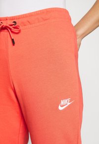 Närbild av korallfärgade Nike-sweatpants med dragsko i midjan och vit broderad Nike-logga på låret, bärs med en vit topp.