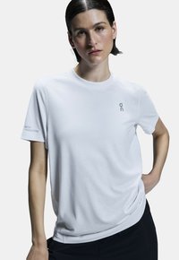 Vit kortärmad t-shirt, rund halsringning, mjukt tyg med "on"-logotyp och texten "SWISS ENGINEERING" på vänster ärm. Designad för komfort.