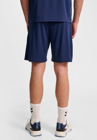 Granatowe krótkie spodenki sportowe z oddychającego materiału z elastycznym paskiem w talii. Uzupełnione białymi skarpetkami do kostek i jasnymi trampkami.