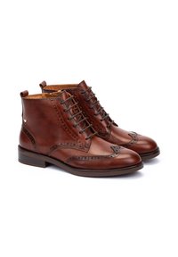 Bottines en cuir marron avec des détails brogués, à lacets sur le devant, à bout arrondi et à petit talon. Présente une finition lisse et une légère texture.