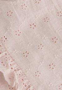 Ljust rosa tyg med blommig broderi och utskurna detaljer. Fläktkant l�ängs sömmen ger textur och en dekorativ element.