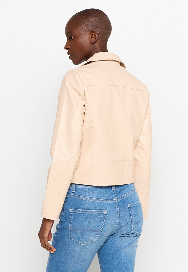 Chaqueta de cuero beige con un diseño ajustado y cuello recto, que presenta un respaldo limpio y una costura minimalista, combinada con jeans azules.