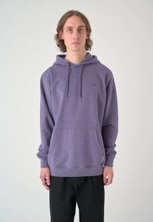 Lila Kapuzenpullover aus weichem Material, mit einer Fronttasche, einer verstellbaren Kapuze und einem dezenten Logo-Akzent. Kombiniert mit schwarzen Hosen.