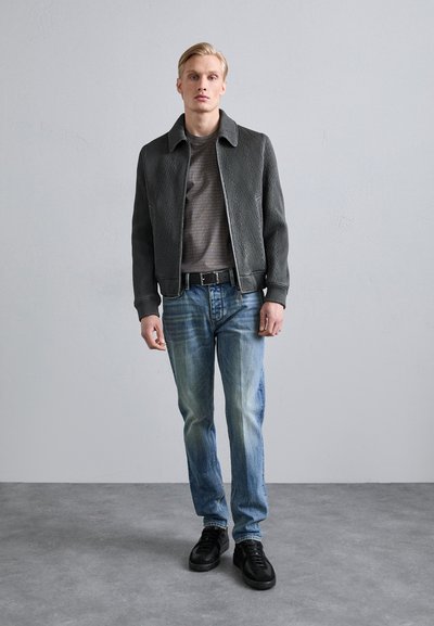 Gray ribbed jacket with a notch collar, paired with a textured gray shirt and light blue jeans. Black sneakers complete the outfit.