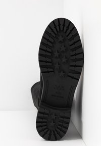 Semelle de bottes noire avec une adhérence texturée, présentant des motifs en forme d'étoiles. Le matériau semble caoutchouteux avec des indications de marque et de taille visibles.