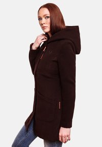Manteau à capuche marron avec fermeture éclair, deux poches avant, un tissu texturé et un logo brodé. La conception présente une coupe ajustée.