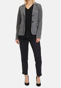 Grå strukturerad kavaj med svarta knappar, slagkrage och sidofickor, matchad med en svart topp och åtsittande svarta byxor.