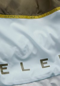 Lyseblåt og gråt stof med en glat tekstur; har guld bogstaver, der stavler "ELEMENTS" og et gult bånd som accent.