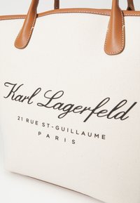 Bijela platnena torba s smešnim kožnim ručkama. Sadrži crni natpis: "Karl Lagerfeld," "21 RUE ST-GUILLAUME," i "PARIS."