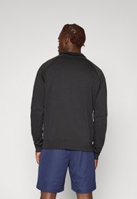 Sort langærmet sweatshirt med høj krave og ribbet kant, parret med blå shorts. Har kontrasterende detaljer på skulderen.