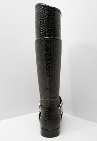 Bottes noires montantes en cuir à motif crocodile texturé en haut et un panneau lisse en dessous, accentuées par une boucle en métal.