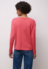 Pull en maille corail à manches longues et coupe décontractée, avec ourlet et poignets côtelés. Associé à un jean bleu.