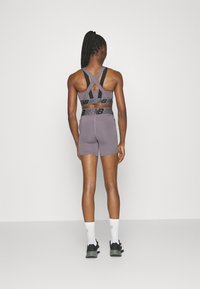 Szary sportowy kombinezon z czarnymi paskami i paskiem w talii, o dopasowanym kroju i krótkich nogawkach. Tekstura wydaje się gładka i elastyczna.