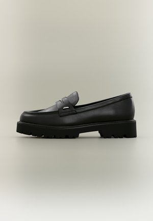 Mocassin en cuir noir avec semelle à crampons épaisse et détail de bride, vu de côté sur un fond neutre.
