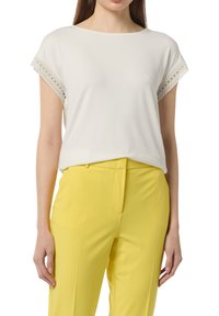 White short-sleeve top with lace trim on sleeves, paired with yellow pants. Top has a relaxed fit and round neckline.