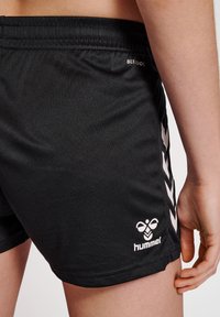 Black athletic shorts made of smooth fabric, featuring a white Hummel logo and chevron pattern on the sides. Elastic waistband for comfort.