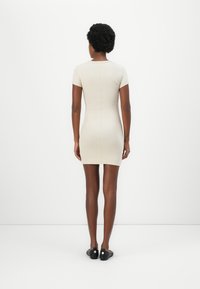 Beige fitted dress with short sleeves and a round neckline, featuring a seam down the back and worn with black slip-on shoes.
