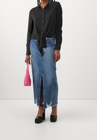 Schwarzes Hemd mit Knöpfen und gebundenem Saum, kombiniert mit einem lässigen blauen Jeansrock mit Frontschlitz. Mit einer pinken Handtasche accessoriert.